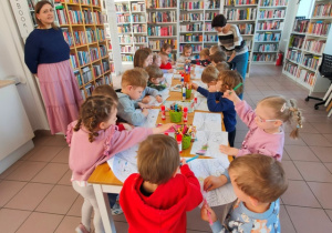 Dzieci przy stolikach kolorują kredkami obrazek.
