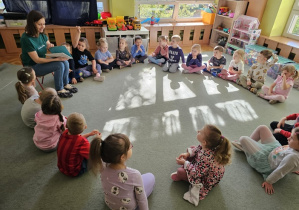 Dzieci siedzą na dywanie a Pani Karolina czyta bajkę