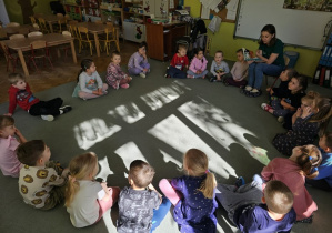 Dzieci siedzą na dywanie i zaciekawieniem słuchają czytanej bajki o kotku
