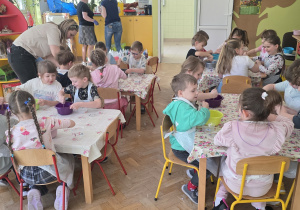 Dzieci pracują przy stolikach, mieszają ze sobą różne składniki potrzebne do zrobienia slajma.