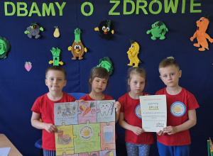 Pamiątkowe zdjęcie dzieci z dyplomem i plakatem przed dekoracją.