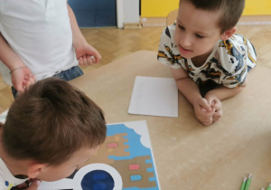 Chłopcy pracują w małych zespołach i wyszukują wskazówek z wykorzystaniem lup.