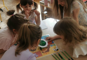 Dziewczynki pracują w małych zespołach i wyszukują wskazówek z wykorzystaniem lup.