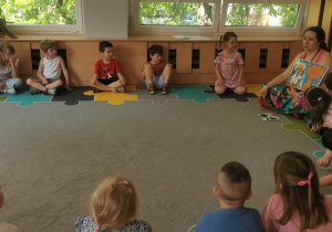 Dzieci siedzą w kole i rozmawiają z muzealnikiem.