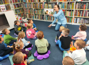 Pani bibliotekarka pokazuje dzieciom książkę, która wprowadzi dzieci w temat spotkania.