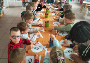 Dzieci kolorują kredkami domek pszczółek.