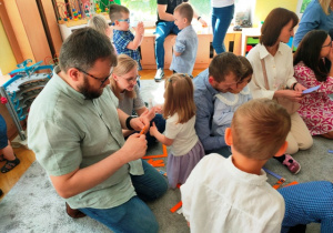 Rodzice składają sklejone paski papieru w harmonijkę tworząc nóżki balonowej świnki.