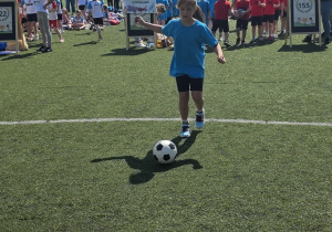Dziewczynka bierze udział w sportowych zmaganiach - kopie piłkę do wyznaczonego celu.