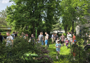 Rodzice wspólnie z dziećmi poszukują ukrytych emblematów grup w magicznym ogrodzie.