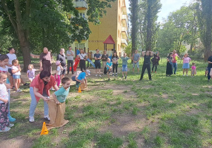Dzieci i rodzice skaczą w workach. Rywalizują grupowo. Pozostali kibicują.