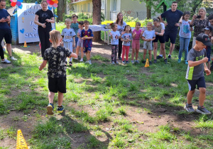 Dzieci wykonują zadanie z jajkiem. Rywalizują grupowo. Pozostali kibicują.