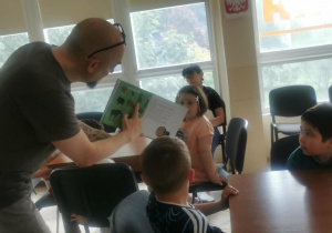 Pan bibliotekarz pokazuje dzieciom ilustracje z leśnymi zwierzętami.