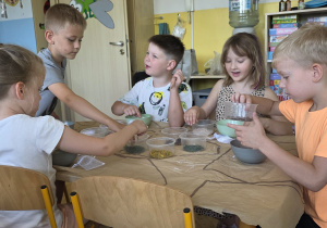 Dzieci pracują przy stolikach, mieszają sól do kąpieli z płatkami kwiatów, ziołami oraz aromatycznymi olejkami eterycznymi.