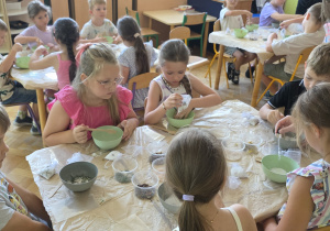 Dzieci pracują przy stolikach, mieszają sól do kąpieli z płatkami kwiatów, ziołami oraz aromatycznymi olejkami eterycznymi.