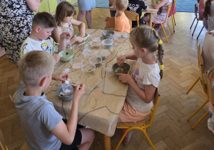 Dzieci pracują przy stolikach, mieszają sól do kąpieli z płatkami kwiatów, ziołami oraz aromatycznymi olejkami eterycznymi.