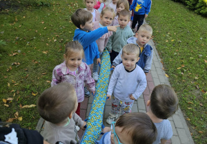 Dzieci trzymając węża idą zwiedzać przedszkolny ogród.