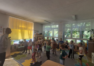 Dzieci stoją w rozsypce na dywanie i naśladują Pana Darka.