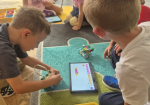 Dzieci bawią się swoimi robotami na dywanie.