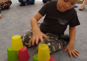 Chłopiec układa wieże z kolorowych kubeczków według wozru.