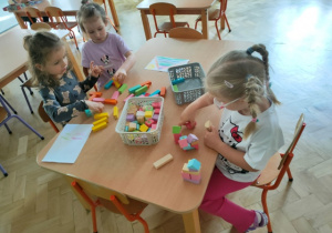 Dziewczynki bawią się przy stoliku klockami drewnianymi.