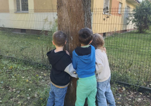 Dzieci przytulają sie do drzewa.