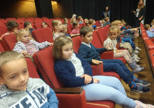 Dzieci siedzą na fotelach teatralnych w oczekiwaniu na spektakl.