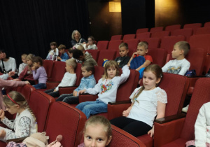 Dzieci siedzą na fotelach teatralnych w oczekiwaniu na spektakl.