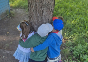 Dzieci przytulają się do drzewa w ogrodzie przedszkolnym.