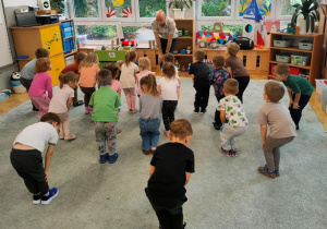 Dzieci stoją w rozsypce na dywanie, rozgrzewają kolana.