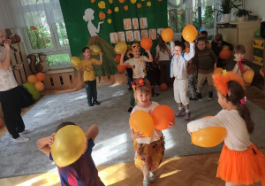 Dzieci tańczą z pomarańczowymi balonami.