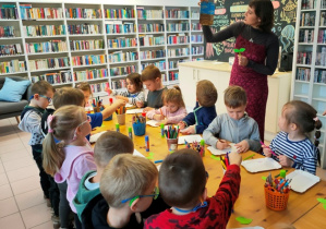 Pani bibliotekarka wyjaśnia dzieciom jak wykonać pracę plastyczną.