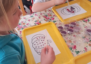 Dzieci siedzą przy stolikach i wykonują dynię.