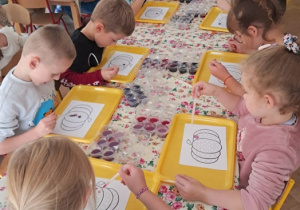 Dzieci siedzą przy stolikach i wykonują dynię.