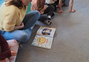 Dzieci siedzą na dywanie i słuchają opowiadania.