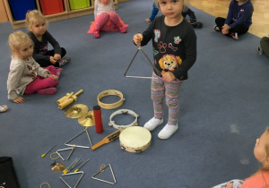 Dzieci siedzą na dywanie obok nich rozłożone są instrumenty, Iga prezentuje trójkąt