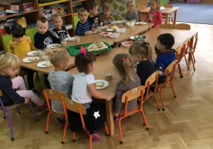 dzieci z grupy pszczółki siedzą przy złączonych stolikach i będą jedli wspólne śniadanie w stylu szwedzkiego stołu