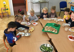 Dzieci siedząc wokół stołu same przygotowują sobie kanapki
