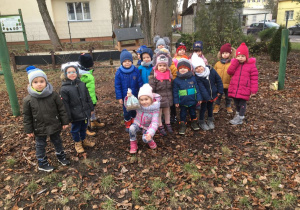 dzieci z grupy Pszczółki stoją w rzędzie w ogródku przedszkolnym i pozują do zdjęcia
