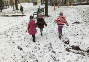 Trzy dziewczynki spacerują po śniegu w ogrodzie przedszkolnym