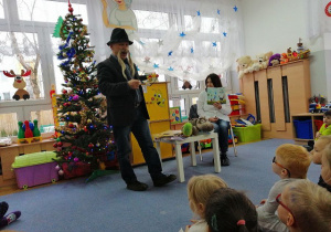 Dzieci siedzą na dywanie a Pan Eugeniusz stoi przed nimi i opowiadam im swoje wiersze