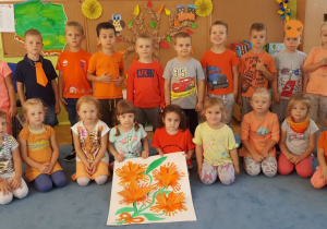 Dzieci ustawione w dwóch rzędach-prezentują swój pomarańczowy bukiet kwiatów.