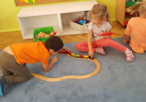 Dwoje dzieci bawi się drewnianą kolejką.