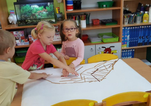 Dzieci budują mrowisko na dużym formacie papieru, przyklejając paski papieru do kartonu.