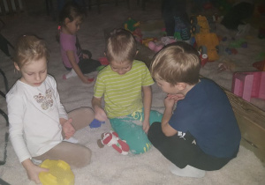 Dzieci siedząc w piaskownicy z solą rozmawiają ze sobą.