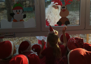 Dzieci patrzą w stronę okna przez które zagląda Mikołaj.