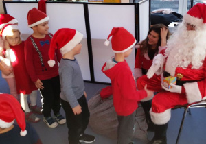 Mikołaj wręcza upominki dzieciom ustawionym w rzędzie.