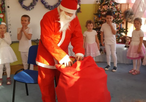 Oczekiwany gość - Mikołaj staje na dywanie z wielkim workiem prezentów.