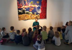 Dzieci oglądają gobelin przedstawiający morską głębinę. Słuchają opowieści przewodnika.