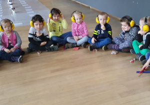 Dzieci z założonymi słuchawkami na uszy słuchają dźwięków oceanu..