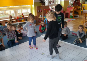 Dzieci chodzą po macie matematycznej rozłożonej na dywanie i szukają najkrótszej drogi aby dojść do żaby.